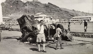 Vehicles destroyed during Arab riots in Aden, 1947. A European man stands by the burnt out shells