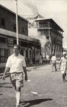 Row of shops destroyed during the riots in Aden, 1947. A European man walks past a row of shops in