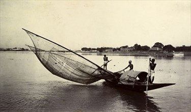 Fishing with a large net, India. Two fishermen steady a small boat with long poles for another who