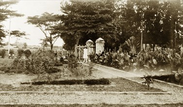 Lagos Club gardens. A European woman in a dress and sun hat stands on a pathway at the entrance to