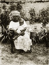 Mother and child, Nigeria. Portrait of a seated African woman holding a baby on her knee. She wears