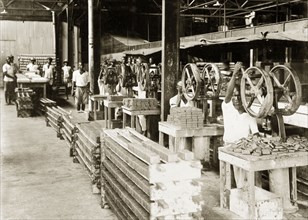 Soap company stamping room. A row of African factory workers stamp bars of soap with hand-operated