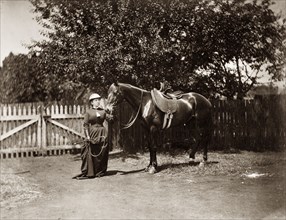 Woman and horse, Australia. A woman dressed in riding habit and helmet holds a horse by the reins