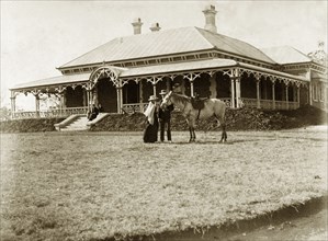 House called 'Wyalla', Australia. A couple with a saddled horse stand on the lawn at 'Wyalla', a