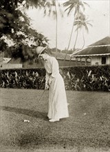 Playing golf, Ross Island. Anne Wood plays golf in the garden of a colonial house. Ross Island,