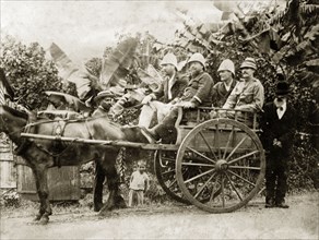 British officials seated in a horse and cart. Four European men in solatopis are seated in a high,