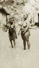 Two women of the Andaman Islands. Two standing women hold hands against a backdrop of a cliff and