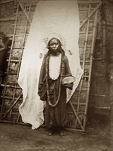 Young mendicant girl. A young female mendicant stands, bowl in hand, dressed in a headdress, a