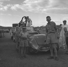 Recovery of a Connaught racing car. A curious group of onlookers gathers to watch the recovery of a