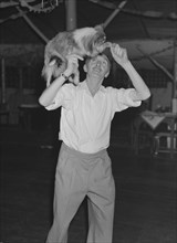 Tom dances with a dog. A man identified as 'Tom', lifts a worried-looking collie dog onto his