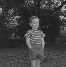 Cheerful boy, Kenya. Stephen Ward stands, hands in pockets, smiling broadly beside a picnic rug