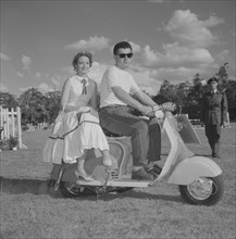 Couple on a scooter. A young couple in typical 1950s Western dress sit on a scooter in a vehicle