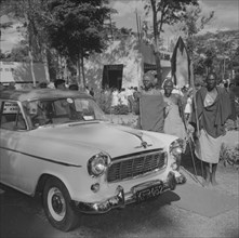 Maasai at Cooper Motors. Three Maasai warriors stand, holding spears, beside a shiny new car on