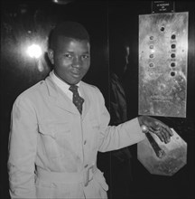Congress House lift attendant. A young African lift attendant smiles for the camera, his hand