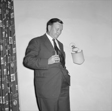 Prudential Insurance cocktail party. A suited businessman leans against the wall, glass in hand, at