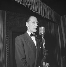 On stage at the Equator Club. A European man stands before a microphone on a small, curtained stage