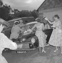 Wedding send off. Female wedding guests surround a car, excitedly throwing confetti over the