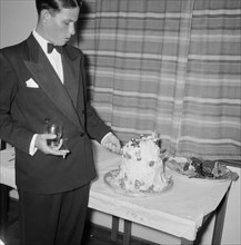 Cutting the cake. A young man dressed in a tuxedo cuts his 21st birthday cake, drink and cigarette