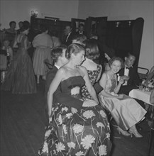Comfortable chair. A young woman in a sleeveless floral party dress sits on a man's knee at the
