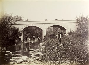 Richmond Bridge, Jamaica. Several people mill about on the banks of a shallow river beneath the