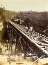 Railway viaduct, Jamaica. Two men stand barefoot on a newly completed trestle bridge built across a