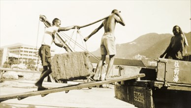 Asian workers, Kowloon. Asian workers carry a heavy load up a ramp onto the back of an open truck.