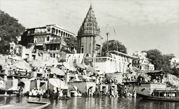 Hindu temple at Benares. Religious pilgrims sit beneath large umbrellas at a ghat (stepped wharf)
