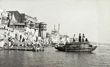 A bathing ghat at Benares. A boat on the River Ganges floats beside a religious bathing ghat