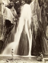 Waterfall, India. Two men in European dress view a waterall from the rocks at its base. India,