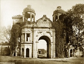 Gateway to the Sikanderbagh. An ornate gateway, partially covered by vegetation, features the fish