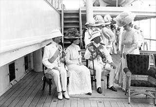 Queen Mary with dignitaries. Queen Mary joins a group of seated dignitaries on the deck of HMS