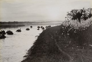 Return to camp. Mounted on elephants, King George V's royal hunting party crosses a river at sunset
