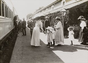 Queen Mary greets children. Shaded by her parasol, Queen Mary greets European children on a railway