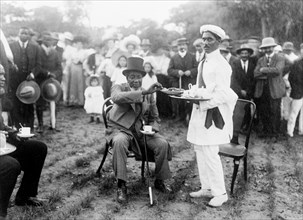 Tea and cake at a royal reception. Dressed in a Western-style suit and top hat, an African chief
