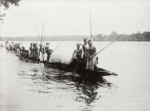 Canoes near Kandahar Island. A group of semi-naked men wearing traditional dress and headgear,