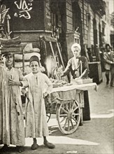 Street peddler, Cairo. A street peddler sells food from a cart whilst two boys in traditional dress