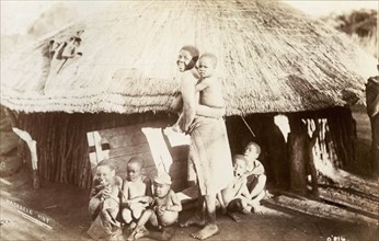 A Matabele family. A Matabele (Ndebele) woman turns to smile for the camera, a young child clinging