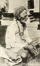 An elderly fakir. Portrait of an elderly fakir sitting cross-legged on a wall. Dressed in a short