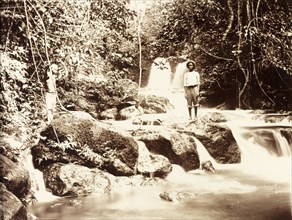 Jungle river in Bioko. Two young men stand on a rock formation straddling a jungle river. The slow