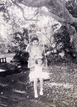 Children on a swing, India. Two British children play on a garden swing. Both wear fancy dress: the