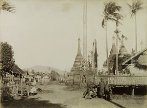 Street scene in Wuntho. A group of Wuntho townspeople mill about outside a shrine containing carved