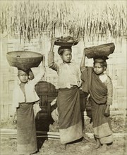 Three Burmese girls at Wuntho. Three young Burmese girls pose outside a thatched dwelling,