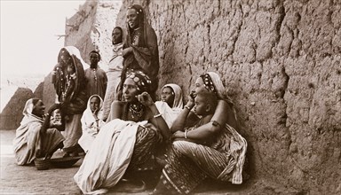 Sudanese women in Omdurman. A group of Sudanese women crouch and stand together beside a high mud