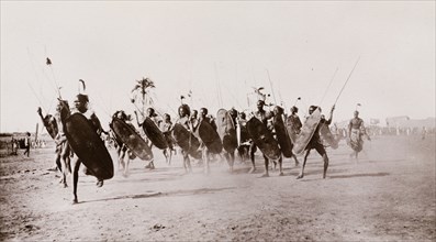 Shilluk warriors charge. A group of Shilluk warriors charge along a dusty plain carrying shields