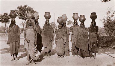 Sudanese women carrying water. A group of Sudanese women, dressed in long robes and headscarves,