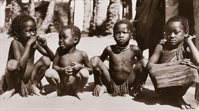 Four Sudanese children. Four semi-naked Sudanese children squat on the ground in a line. Their hair