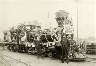 Royal train at Perth. Two men stand beside a locomotive, decorated with flowers and bunting for the