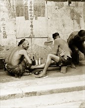 A medicine stall in Hong Kong. A man wearing a traditional Manchu hairstyle squats beside a row of