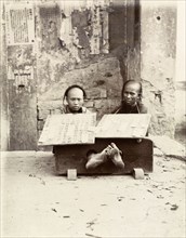 Petty criminals in the stocks, Hong Kong. Two petty criminals sit with their ankles restrained in