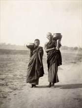 Pot carriers in Mandalay. A Burmese man and a boy dressed in long robes carry pots on their